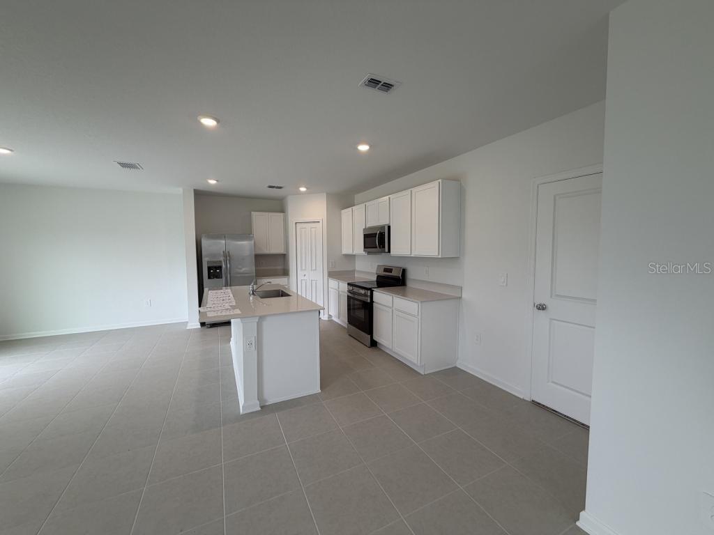 A kitchen features white cabinets, stainless steel appliances, a center island, and tile flooring — 2510 HALLOW GRADEN RD, EUSTIS, FL