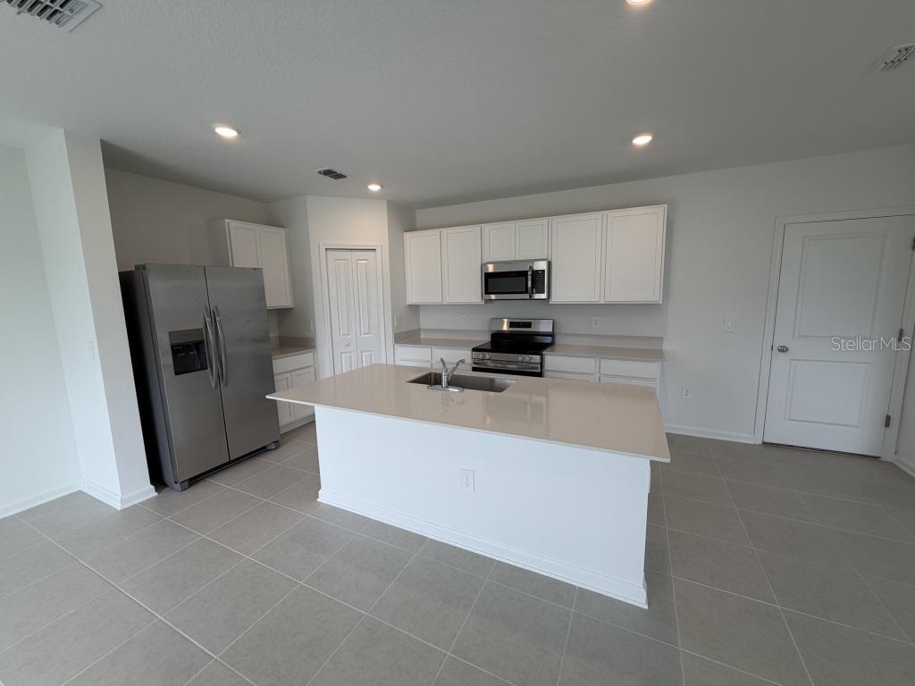 A kitchen features white cabinets, stainless steel appliances, a center island, and light-colored tile flooring — 2510 HALLOW GRADEN RD, EUSTIS, FL