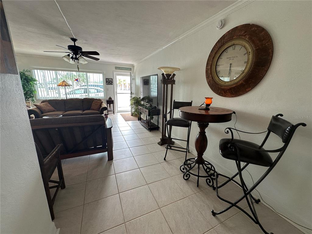 A living room features tile flooring, a ceiling fan, a large wall clock, and furniture — 6161 GULF WINDS DRIVE UNIT 150, ST PETE BEACH, FL