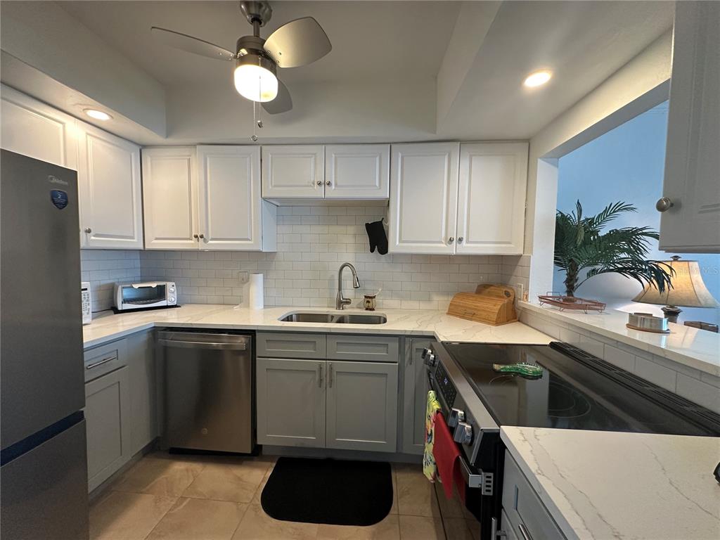 A kitchen with white upper cabinets, gray lower cabinets, stainless steel appliances, and white countertops — 6161 GULF WINDS DRIVE UNIT 150, ST PETE BEACH, FL