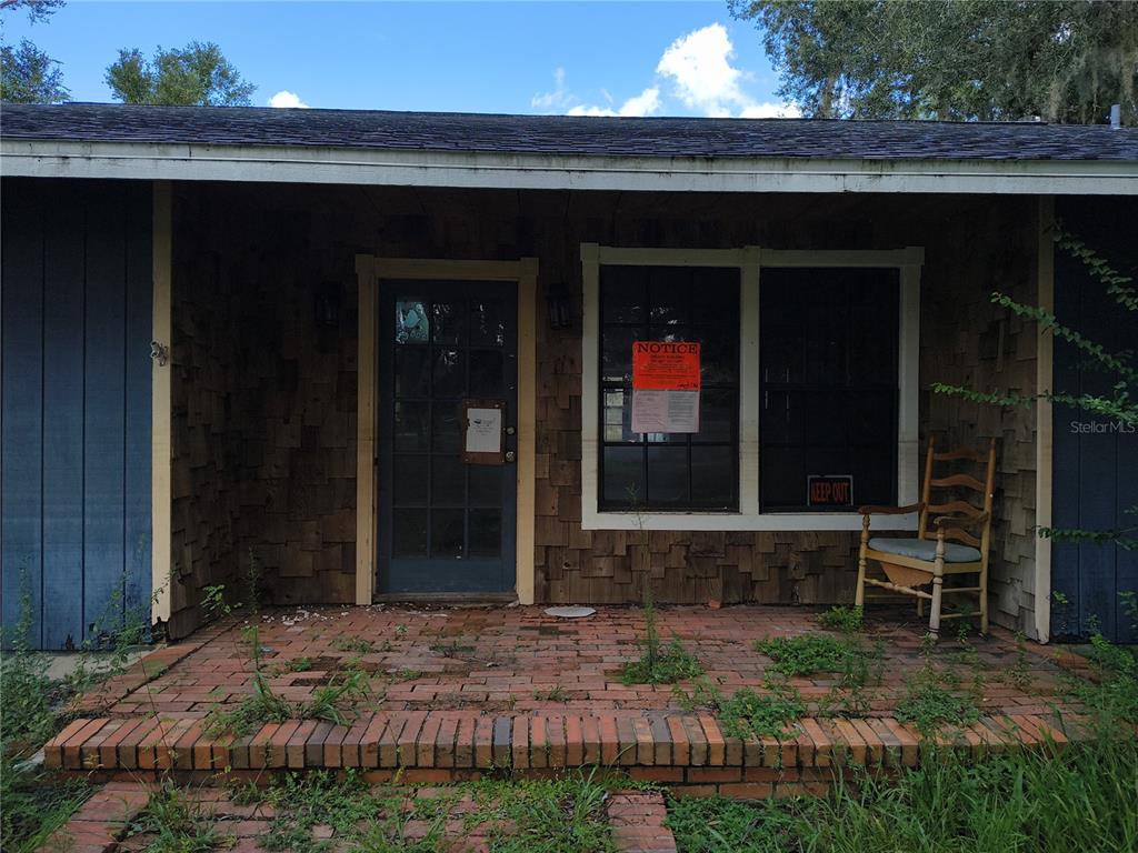 A brick porch with a wooden rocking chair sits in front of a shingled house — 5125 LAKEWOOD DRIVE, DADE CITY, FL