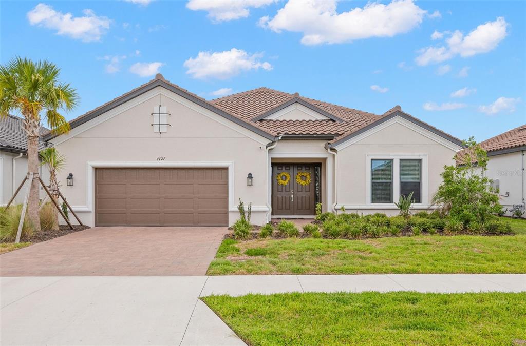 A single-story house with a beige stucco exterior, brown garage door, and tiled roof — 4727 FRECCIA LOOP, WESLEY CHAPEL, FL