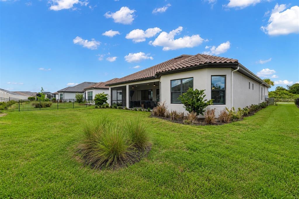 The rear exterior of a single-story house features a screened-in patio and a fenced yard — 4727 FRECCIA LOOP, WESLEY CHAPEL, FL