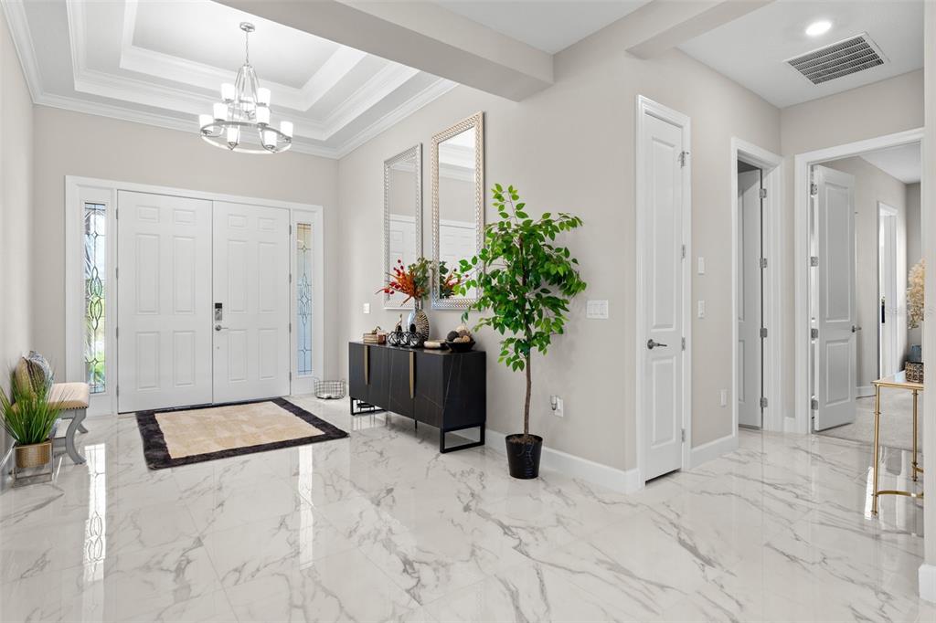 A bright foyer features white marble floors, a tray ceiling with a chandelier, and double doors — 4727 FRECCIA LOOP, WESLEY CHAPEL, FL