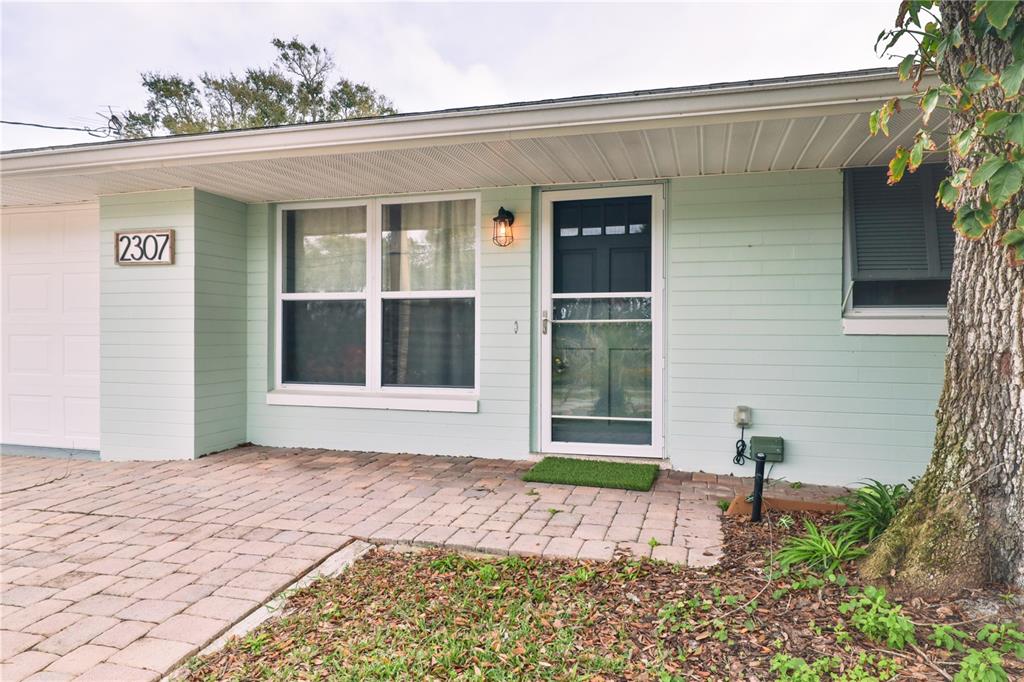 A light green brick house exterior features a paved walkway, a front door, and windows — 2307 SAXON DRIVE, NEW SMYRNA BEACH, FL