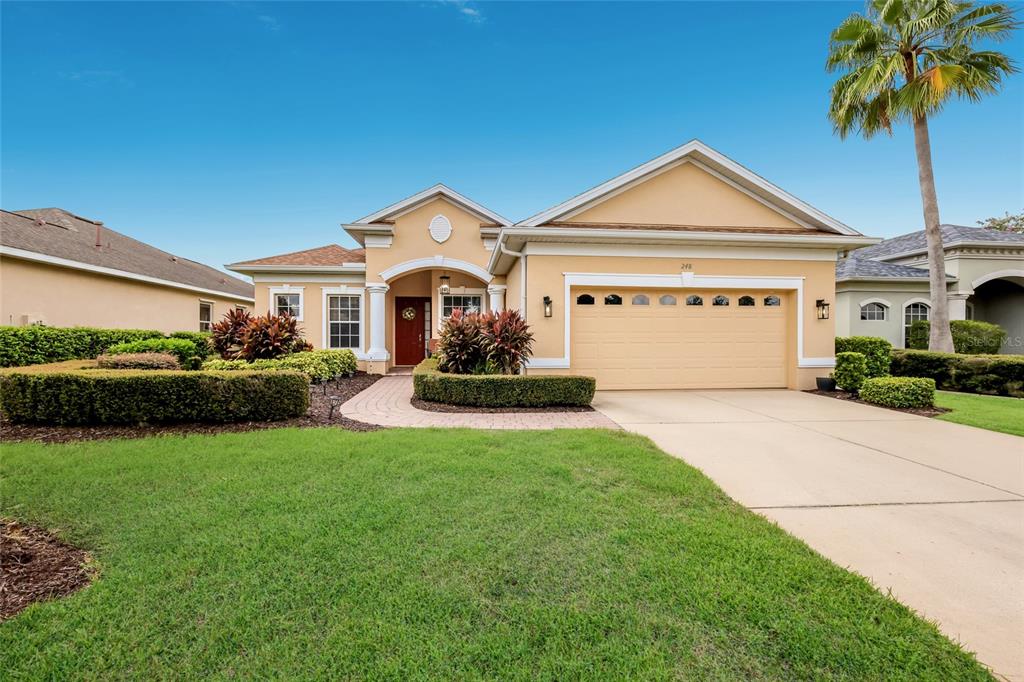 A single-story house with a beige stucco exterior, a two-car garage, and a palm tree — 248 DAHLIA COURT, BRADENTON, FL