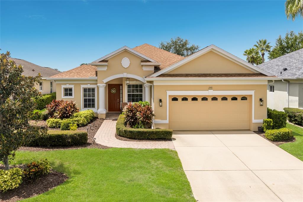 A single-story tan house with a two-car garage, a paved walkway, and manicured landscaping — 248 DAHLIA COURT, BRADENTON, FL
