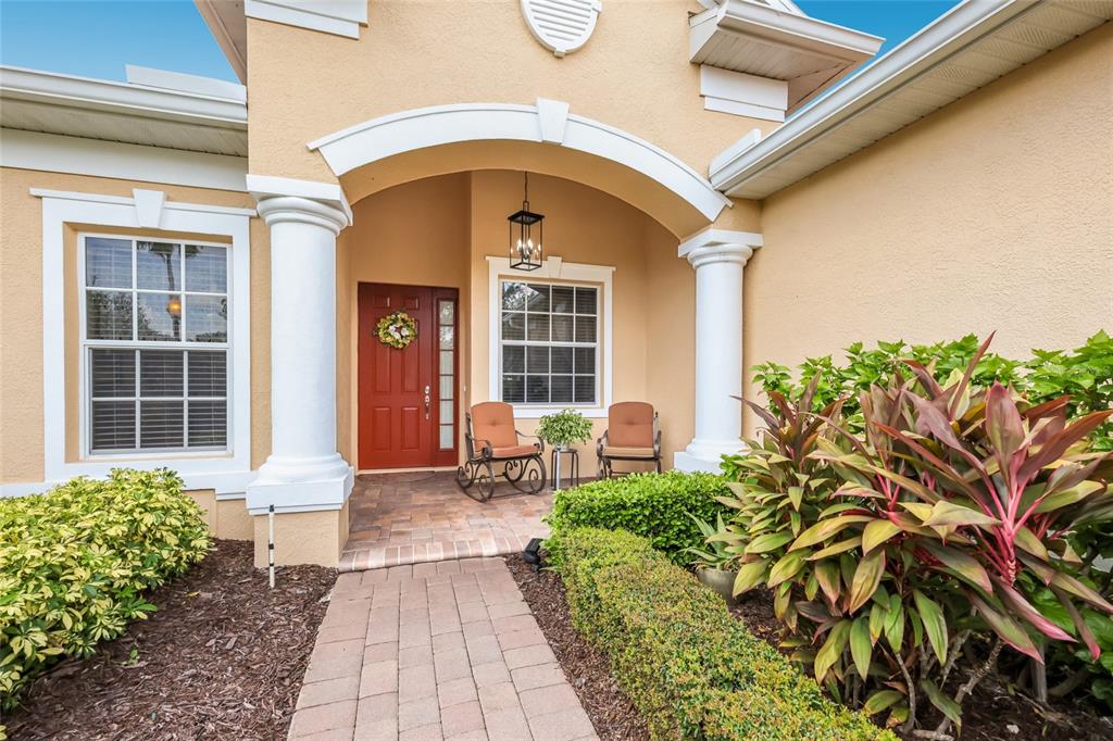 A front entrance with a red door, two rocking chairs, and a paved walkway — 248 DAHLIA COURT, BRADENTON, FL