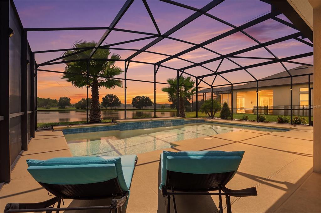 A screened-in pool patio features two lounge chairs overlooking a lake at sunset — 2470 DAMMAR STREET, ORLANDO, FL