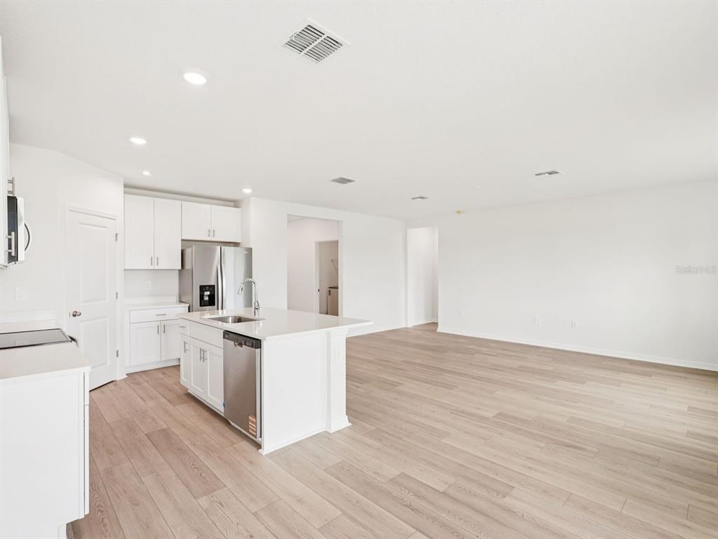 A modern kitchen with white cabinets and a center island opens into a living area — 10437 ABUNDANCE GROVE WAY, PARRISH, FL