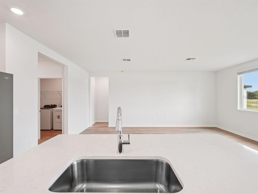 A kitchen island with a stainless steel sink overlooks an open living area and laundry room — 10437 ABUNDANCE GROVE WAY, PARRISH, FL