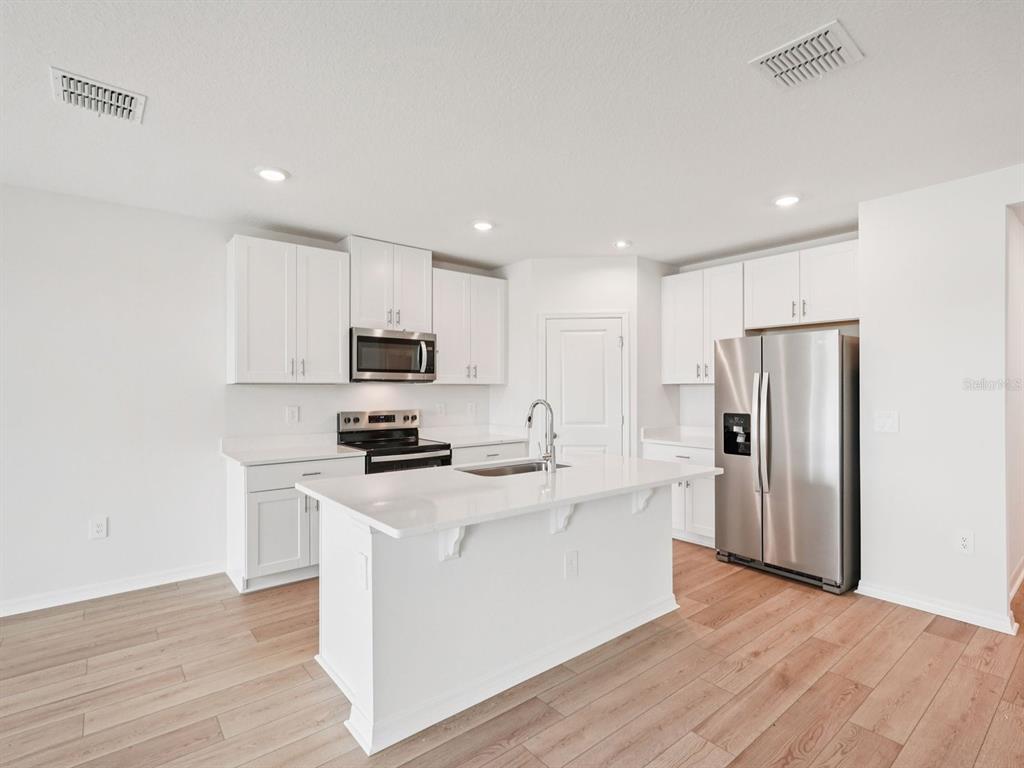 A modern kitchen features white cabinets, stainless steel appliances, a center island, and wood flooring — 10437 ABUNDANCE GROVE WAY, PARRISH, FL