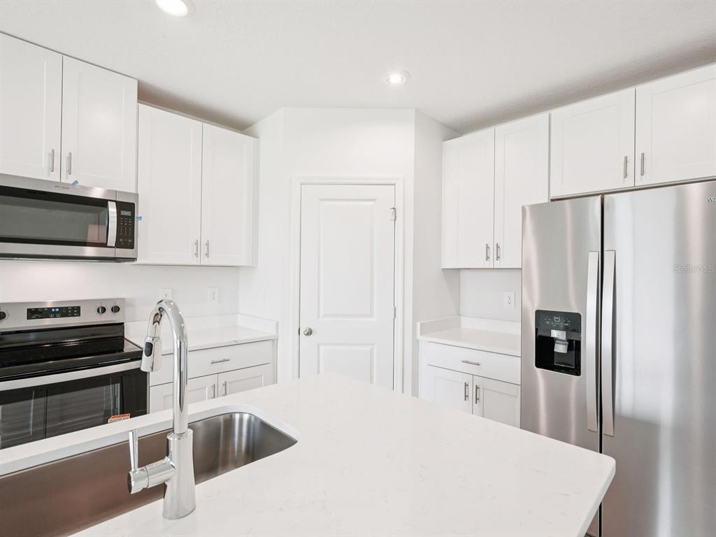 A modern kitchen features white cabinets, stainless steel appliances, and a white quartz island countertop — 10437 ABUNDANCE GROVE WAY, PARRISH, FL