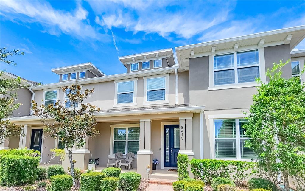 A two-story townhouse exterior features a blue front door, beige stucco walls, and manicured landscaping — 8415 LOVETT AVENUE, ORLANDO, FL