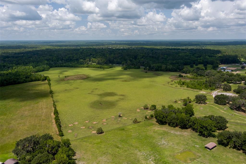 An aerial view of a large, open green pasture surrounded by trees and a blue sky — 9504 NW HWY 320, MICANOPY, FL