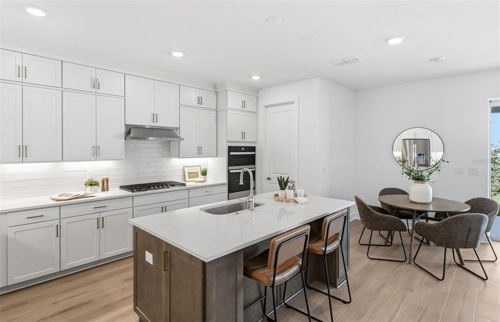 A modern kitchen features white cabinetry, a dark wood island with seating, and an adjacent dining area — 37253 GUNNISON DRIVE, ZEPHYRHILLS, FL