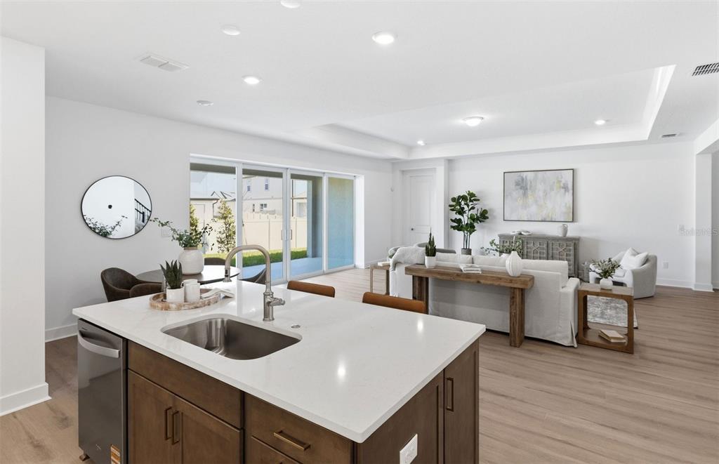A kitchen island with a sink overlooks an open-concept living area with light wood flooring — 37253 GUNNISON DRIVE, ZEPHYRHILLS, FL