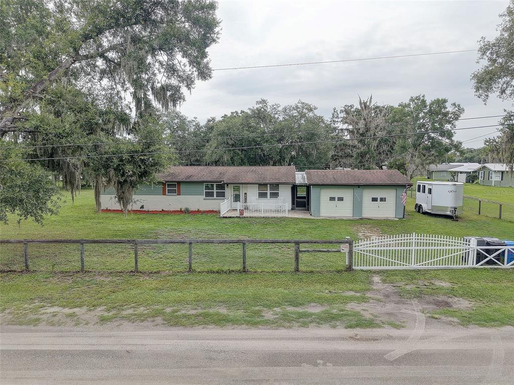 A single-story house with a two-car garage, white fence, and a trailer parked on the lawn — 13102 GIBSON LANE, ODESSA, FL