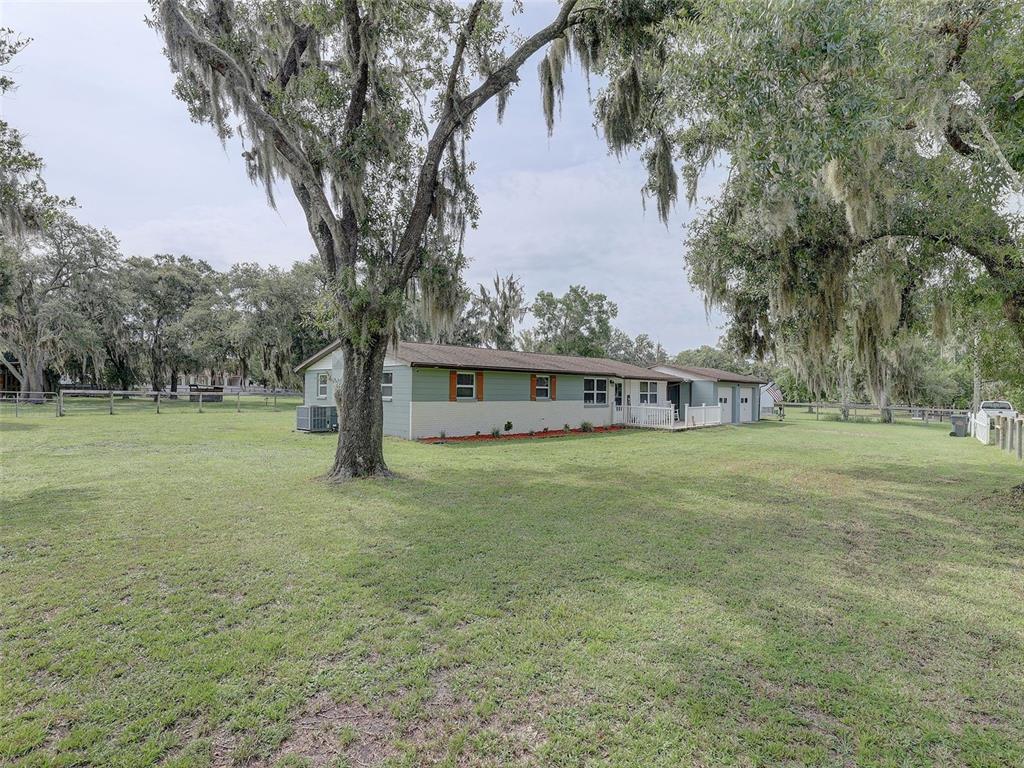 A single-story house with green and beige siding sits on a large, tree-filled grassy lot — 13102 GIBSON LANE, ODESSA, FL