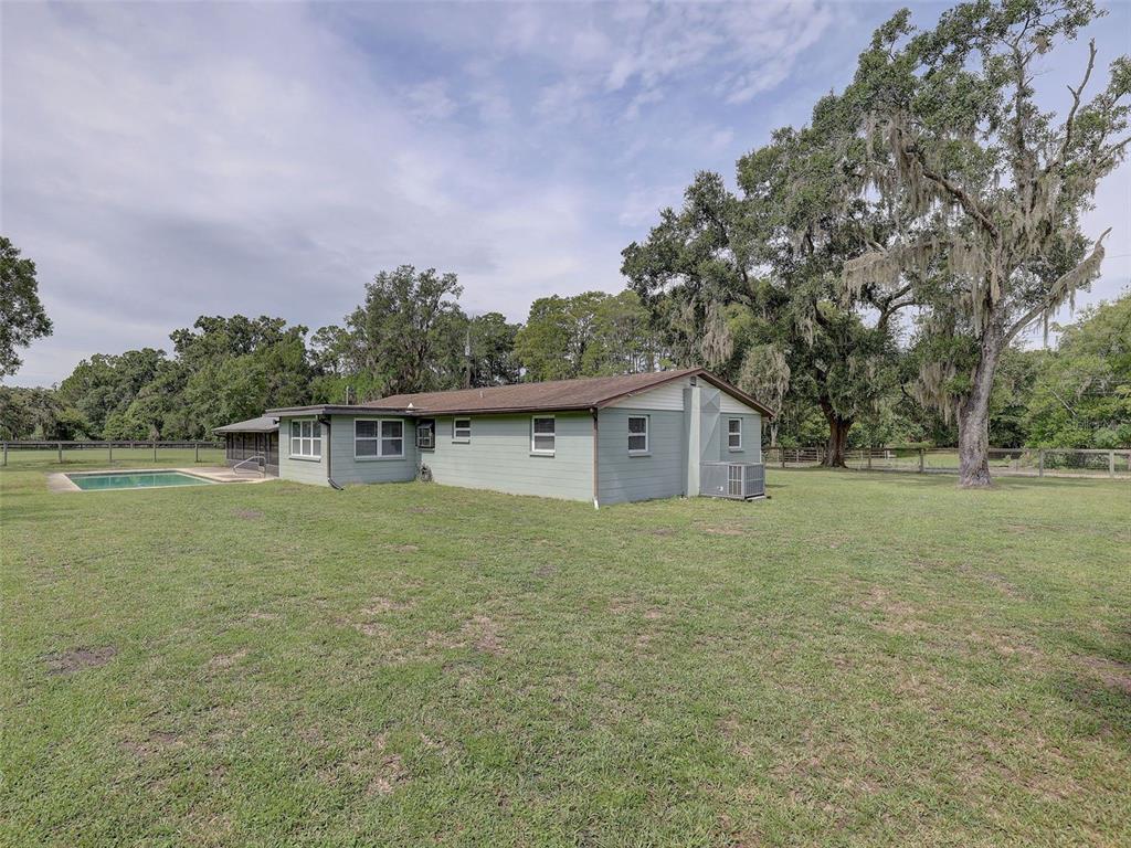 A single-story house with light green siding, a swimming pool, and large oak trees nearby — 13102 GIBSON LANE, ODESSA, FL
