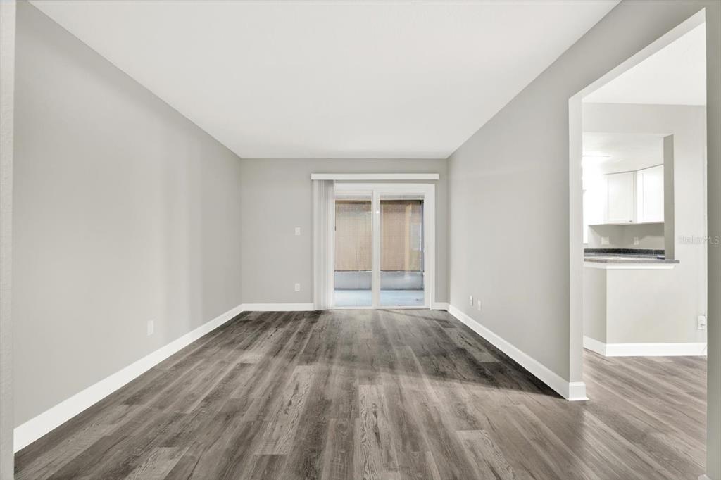 An empty living room features gray wood-look flooring, light walls, and a sliding glass door — 8345 13TH STREET N UNIT B, ST PETERSBURG, FL