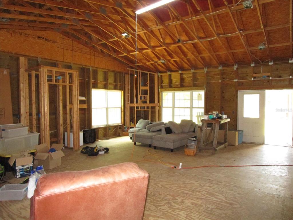 An unfinished room with exposed wood framing, plywood flooring, and a vaulted ceiling — 21108 DURDEN ROAD, DADE CITY, FL