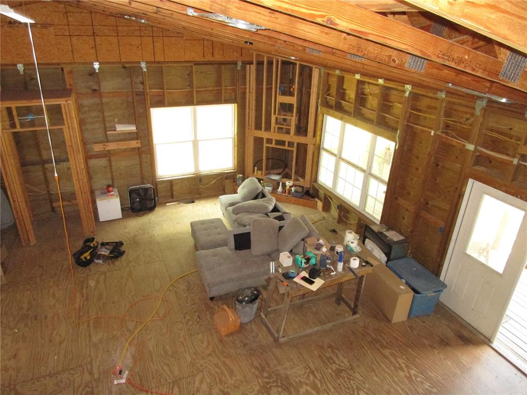 An unfinished room features exposed wood framing, plywood flooring, a sectional sofa, and large windows — 21108 DURDEN ROAD, DADE CITY, FL