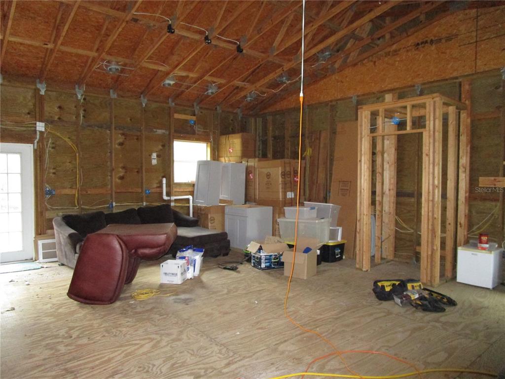 An unfinished room with exposed wood framing, plywood walls, a sofa, and construction materials — 21108 DURDEN ROAD, DADE CITY, FL