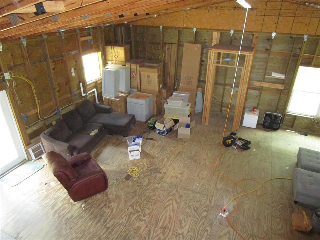 An unfinished room with exposed wood framing, plywood flooring, a brown sectional, and storage boxes — 21108 DURDEN ROAD, DADE CITY, FL