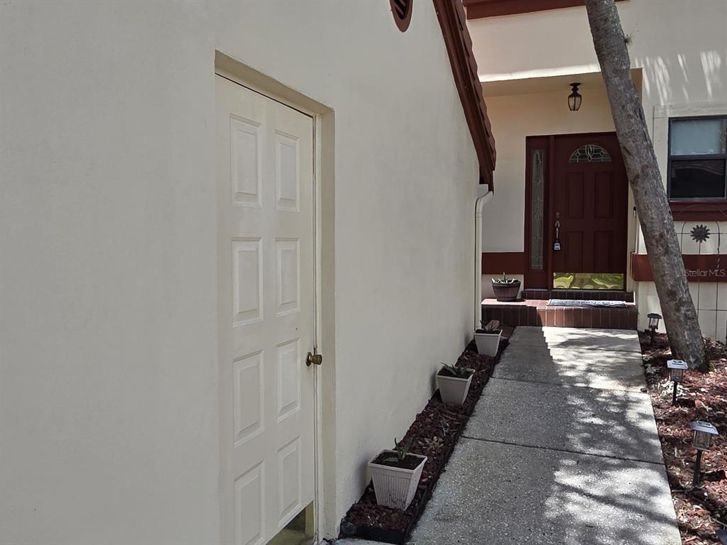 A white door on the side of a house leads to a walkway toward the entrance — 3460 COUNTRYSIDE BOULEVARD UNIT 59, CLEARWATER, FL