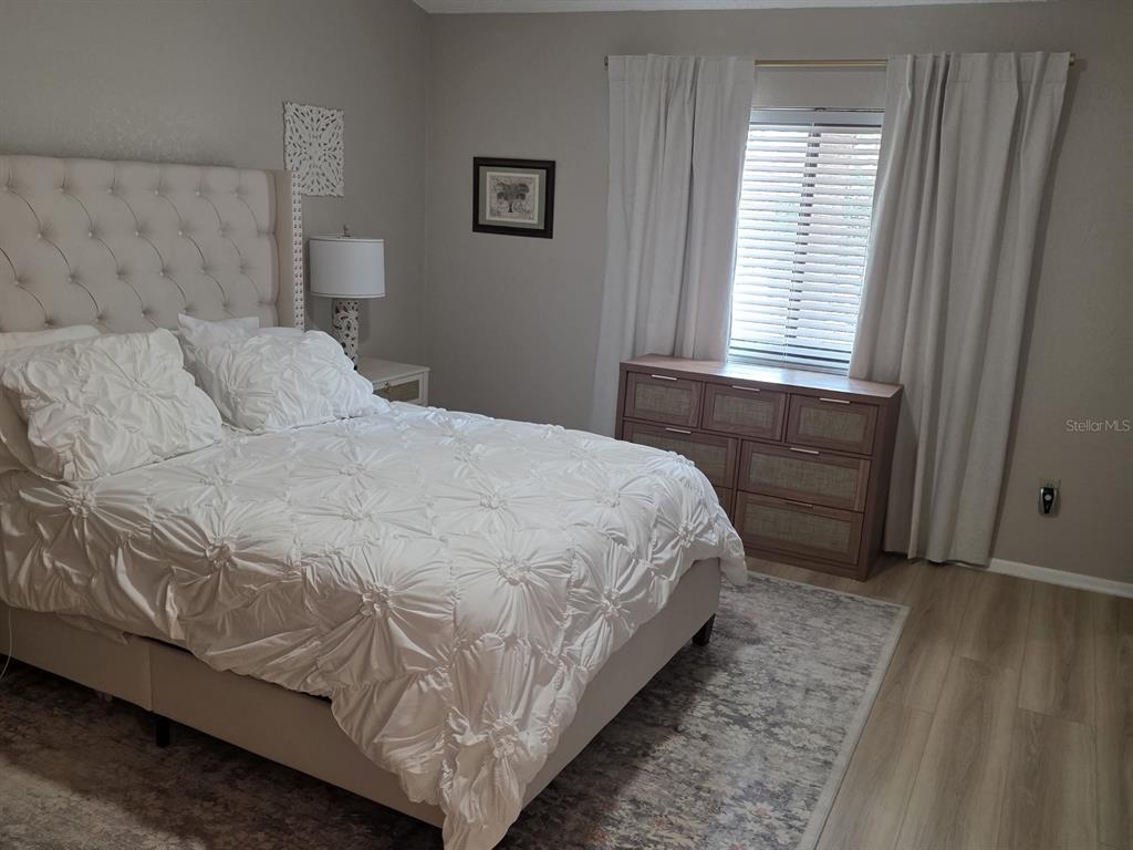 A bedroom features a tufted headboard, white bedding, a wooden dresser, and light wood flooring — 3460 COUNTRYSIDE BOULEVARD UNIT 59, CLEARWATER, FL