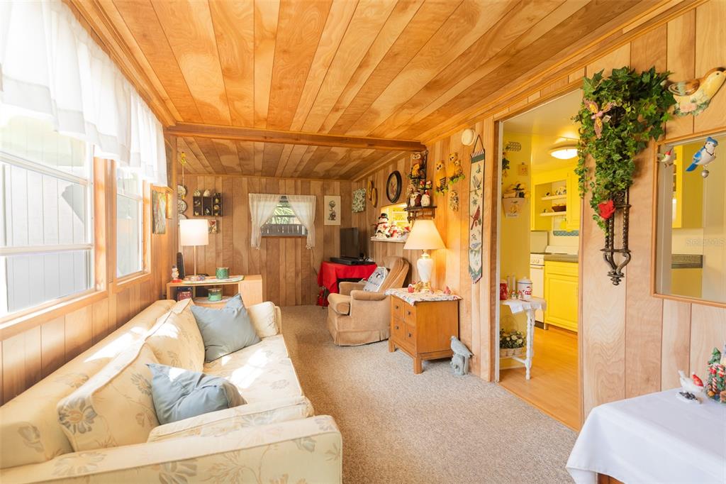 A living room with wood-paneled walls and ceiling, a beige sofa, and a kitchen doorway — 28 BASIN STREET, LORIDA, FL