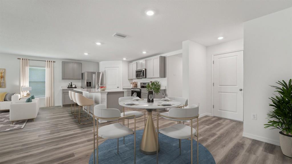 An open-concept kitchen and dining area features light gray cabinetry, stainless appliances, and wood-look flooring — 4330 HIDDEN FARM DRIVE, PLANT CITY, FL