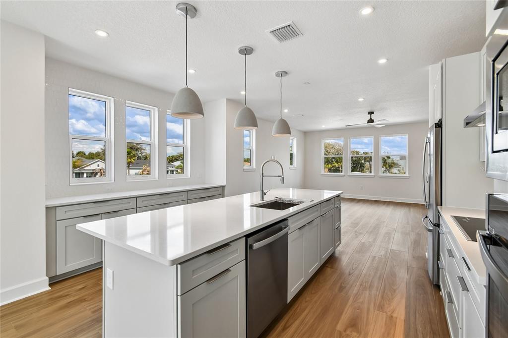 A modern kitchen features a white quartz island, gray cabinetry, and light wood flooring — 4101 TIDEWATCH LOOP, NEW SMYRNA BEACH, FL