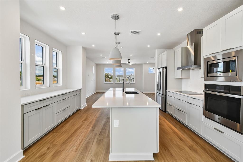 A modern kitchen features white cabinetry, a central island, stainless steel appliances, and wood flooring — 4101 TIDEWATCH LOOP, NEW SMYRNA BEACH, FL