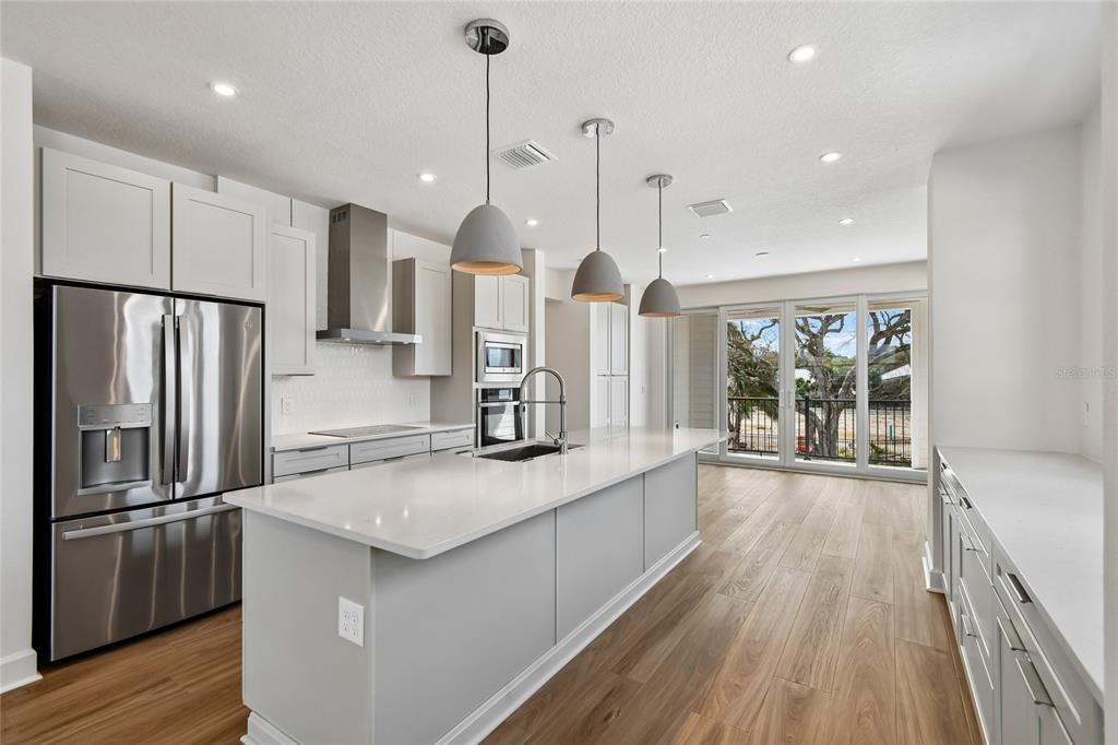 A modern kitchen features a large white island, stainless steel appliances, and light wood flooring — 4101 TIDEWATCH LOOP, NEW SMYRNA BEACH, FL