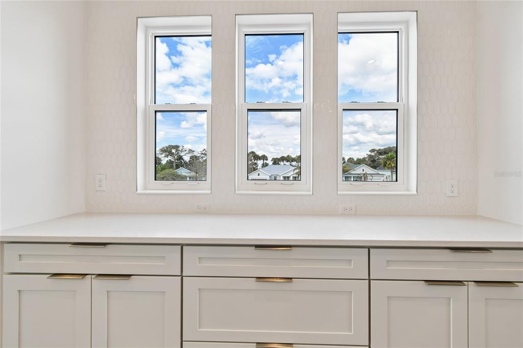 A white kitchen counter with cabinets sits below three windows overlooking a neighborhood — 4101 TIDEWATCH LOOP, NEW SMYRNA BEACH, FL