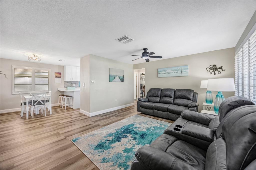 A living room with gray leather sofas, a blue area rug, and an adjacent kitchen — 2155 EDYTHE DR, DUNEDIN, FL