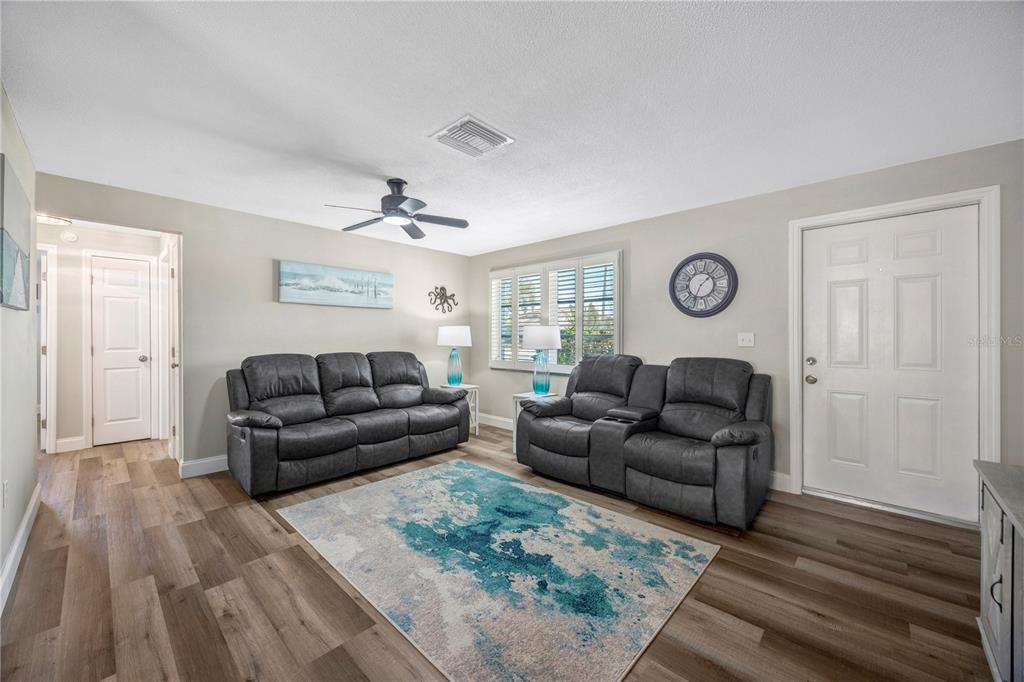 A living room features two gray reclining sofas, a blue patterned rug, and wood flooring — 2155 EDYTHE DR, DUNEDIN, FL