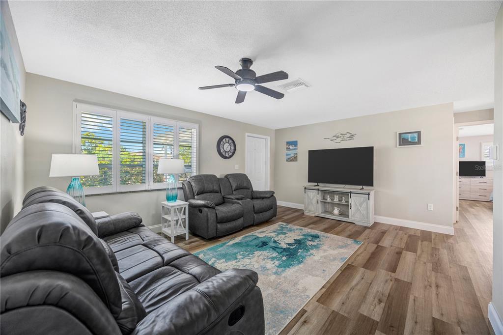 A living room features gray leather sofas, a television on a console, and wood flooring — 2155 EDYTHE DR, DUNEDIN, FL