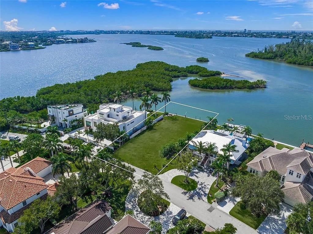 An aerial view shows a vacant waterfront lot situated between two large residential homes — 1386 TANGIER WAY, SARASOTA, FL