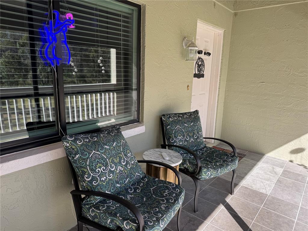 A covered patio features two patterned chairs, a small round table, and a window — 1775 CUPECOY CIRCLE UNIT 4, LUTZ, FL