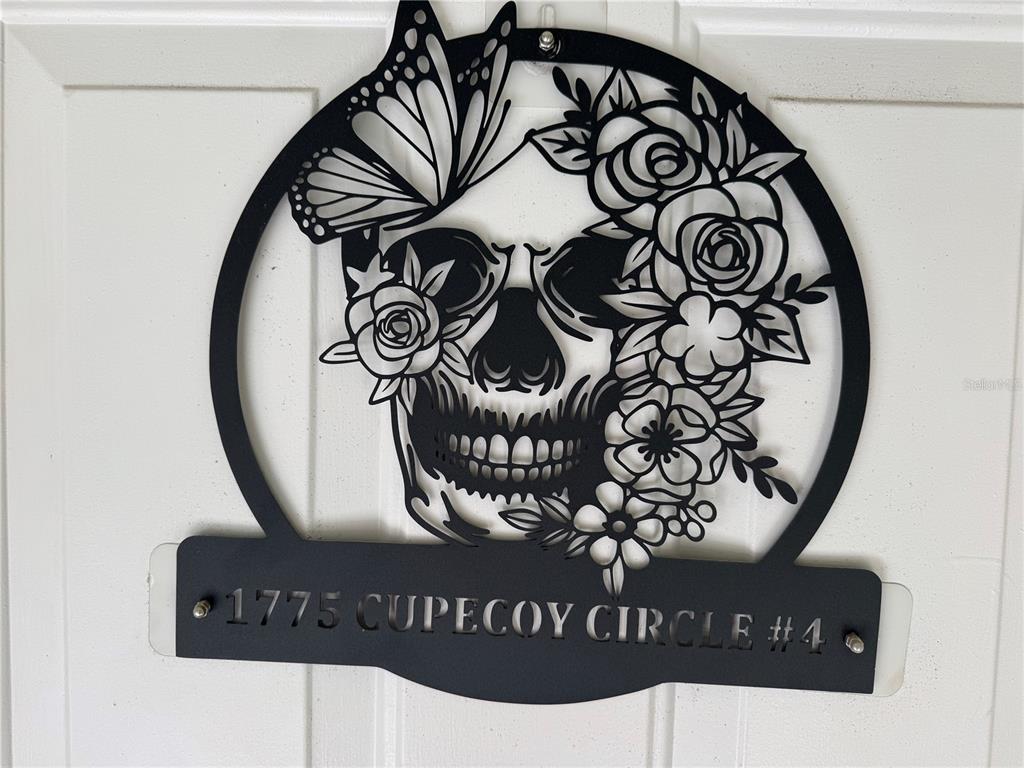 A black metal wall hanging features a skull, flowers, and a butterfly on a door — 1775 CUPECOY CIRCLE UNIT 4, LUTZ, FL