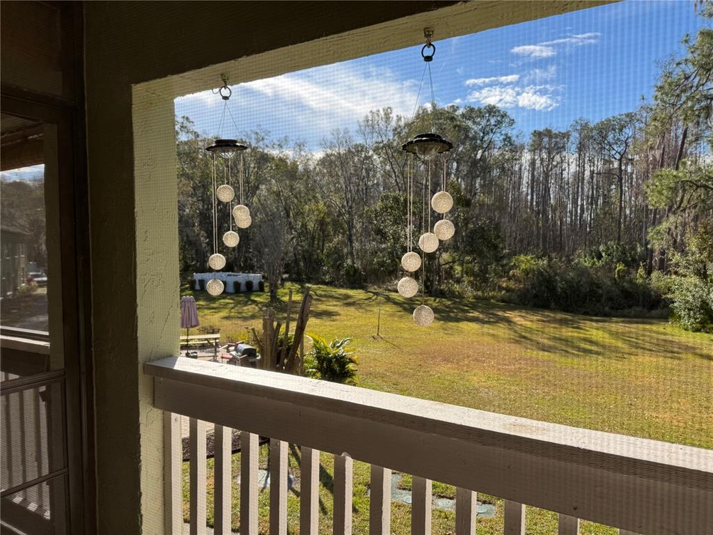 A screened-in porch overlooks a grassy backyard with trees and hanging solar lights — 1775 CUPECOY CIRCLE UNIT 4, LUTZ, FL