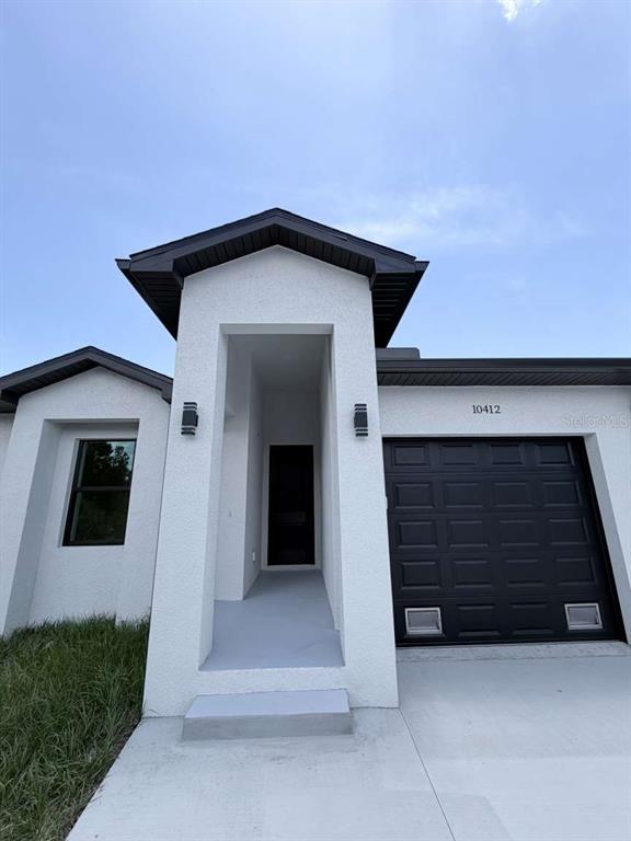 A white stucco house exterior features a black garage door and a recessed front entrance — 10412 PORT EVERGLADES STREET, PORT CHARLOTTE, FL