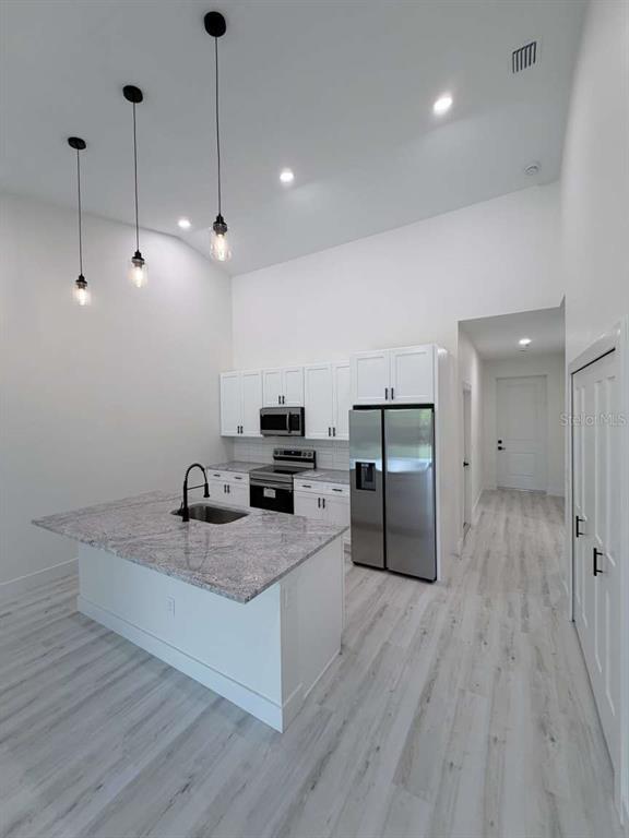 A modern kitchen features a granite-topped island, white cabinetry, stainless steel appliances, and pendant lighting — 10412 PORT EVERGLADES STREET, PORT CHARLOTTE, FL