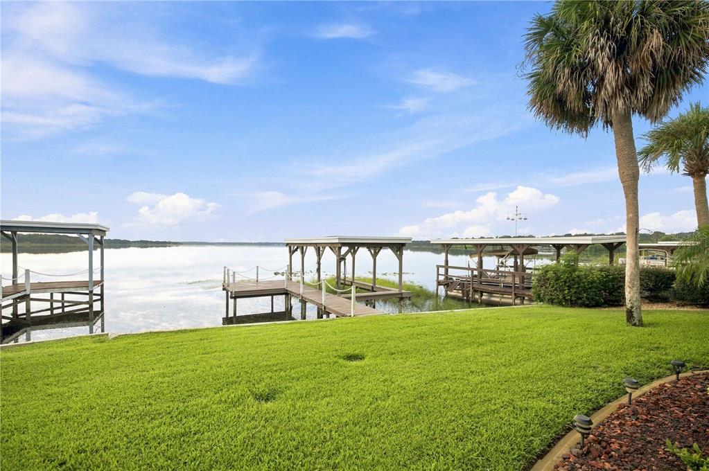 A grassy backyard leads to several wooden boat docks on a calm lake under blue skies — 15 SUNRISE TRAIL, FRUITLAND PARK, FL