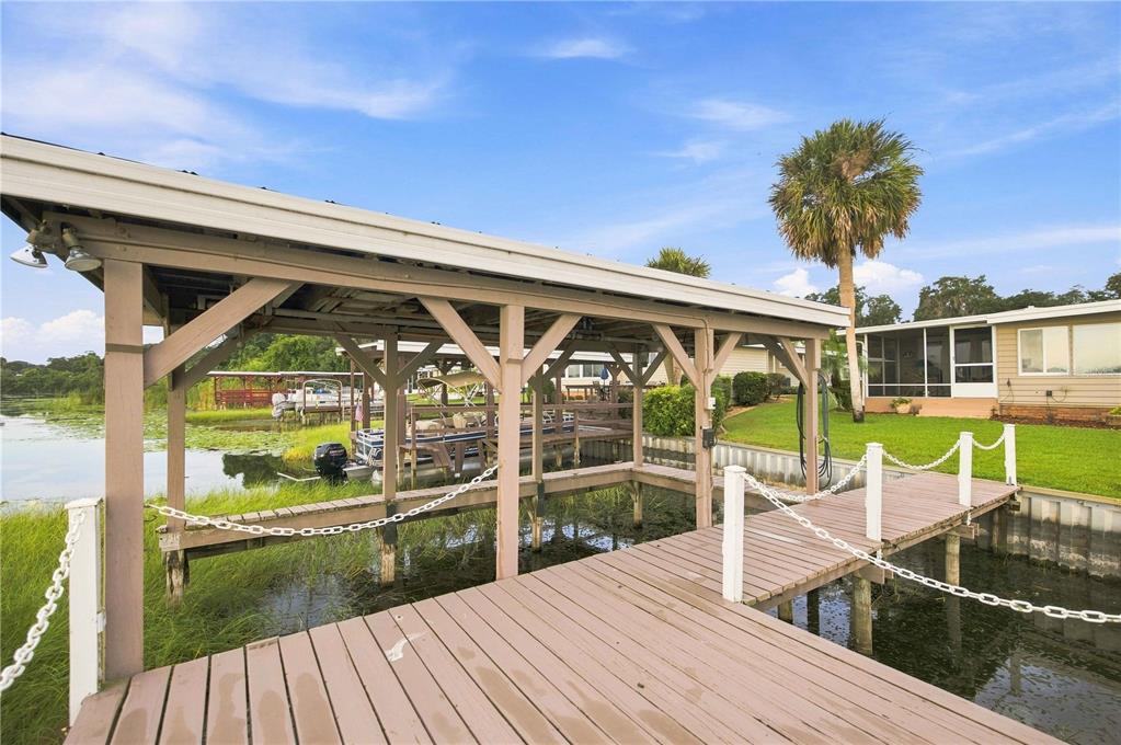 A wooden boat dock with a covered slip extends into a lake near a house — 15 SUNRISE TRAIL, FRUITLAND PARK, FL