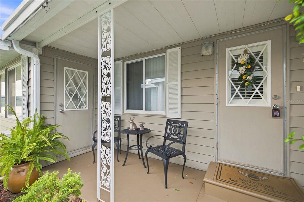 A covered porch features tan siding, two black metal chairs, a small table, and two doors — 15 SUNRISE TRAIL, FRUITLAND PARK, FL
