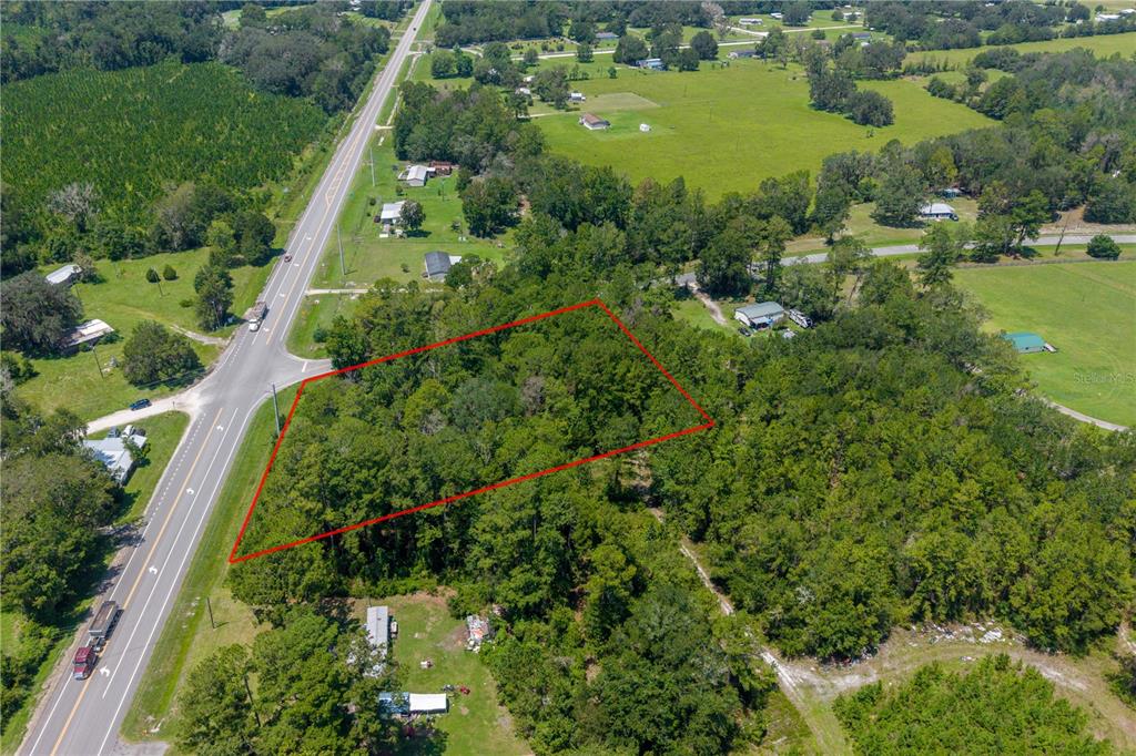 An aerial view shows a wooded, rectangular plot of land outlined in red beside a highway — TBD SR 100, LAKE BUTLER, FL